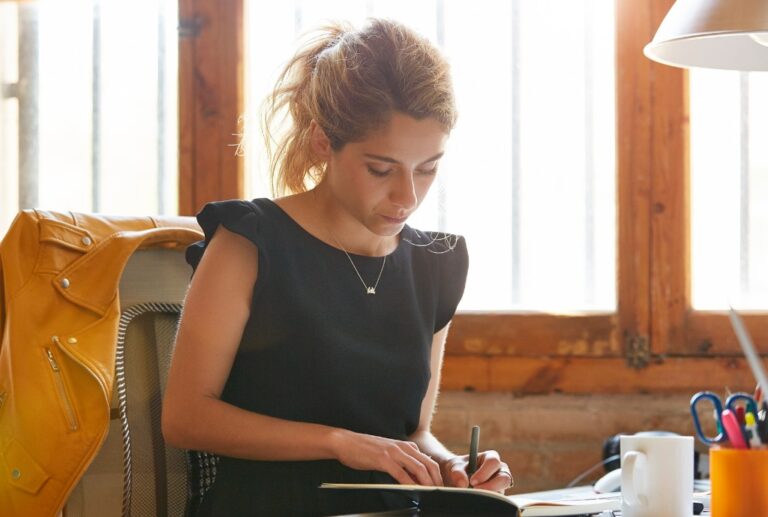 Businesswoman Writing In Book At Desk.jpg S1024x1024wisk20cwpeuk2ckskn8c2td9yxev5mrf4zdq7qgai0df0larsm 1.jpg