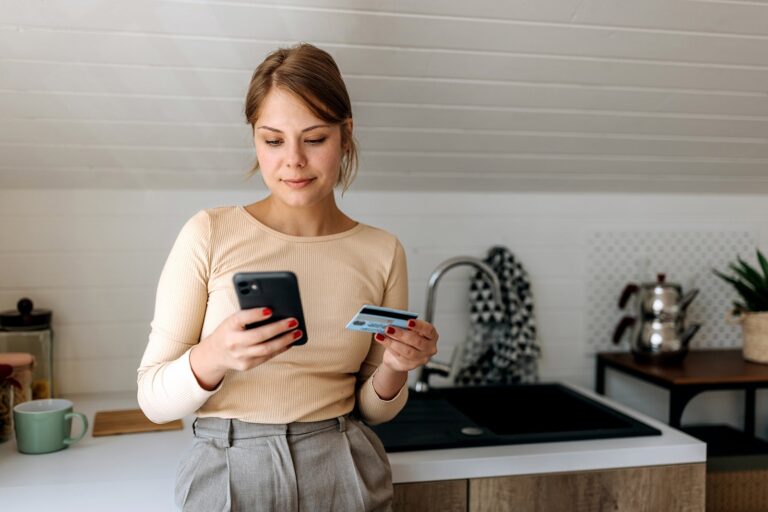 Young woman on her smart phone at home while holding credit card pekic.jpg